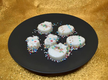 Delicate milky Easter figures made on agar-agar. Decorated with sugar decorations.Dark gray plate. Golden background.