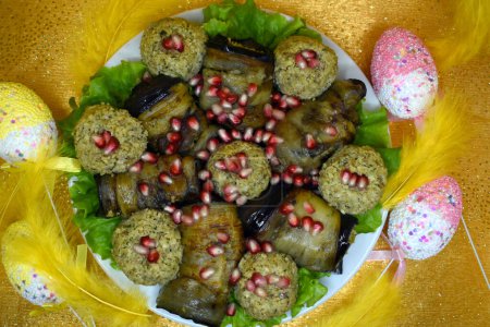 Eggplant rolls stuffed with walnuts and pkhali. Located on green lettuce leaves. Decorated with pomegranate seeds. Gold background.