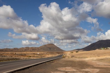 Foto de Camino en un valle a las montañas cerca de la ciudad de Tindaya, centro de la isla. No hay tráfico en la temporada de invierno. Cielo azul con nubes blancas. Fuerteventura, España. - Imagen libre de derechos