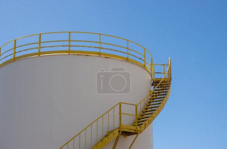 Photo for White tank with yellow staris and railing on the top. Bright blue sky. Part of the industrial zone in the capital city. Puerto del Rosario, Fuerteventura, Canary Islands, Spain. - Royalty Free Image