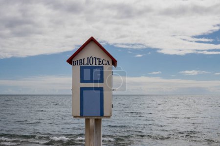 Photo for Little wooden house with title Biblioteca, built on the promenade of Atlantic ocean, to share the books. Blue sky with white clouds. Tarajalejo, Fuerteventura, Canary Islands, Spain. - Royalty Free Image