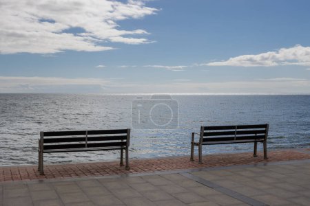 Photo for Promenade at the coast of the Atlantic ocean. Two empty benches to enjoy the view. Blue sky with white clouds. Tarajalejo, Fuerteventura, Canary Islands, Spain. - Royalty Free Image