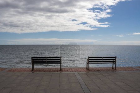 Photo for Promenade at the coast of the Atlantic ocean. Two empty benches to enjoy the view. Blue sky with white clouds. Tarajalejo, Fuerteventura, Canary Islands, Spain. - Royalty Free Image