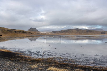 Foto de Agua en un lago que refleja el cielo nublado en el otoño. Lago rodeado de montañas. Dyrholaey, sur de Islandia. - Imagen libre de derechos