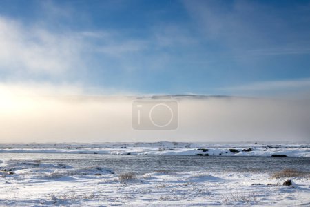El invierno ártico comenzó en otoño y cubrió la tierra con nieve. La base del aire de la cascada está llena de vapor y niebla, en parte ocultando las montañas en el fondo. Fossholl - Godafoss, Islandia.