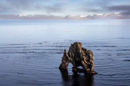 Natural statue close to the coast of the island. Drinking animal, can be dragon or elephant. Calm water of Atlantic ocean. Cloudy sky in the autumn. Hvitserkur, North Iceland.