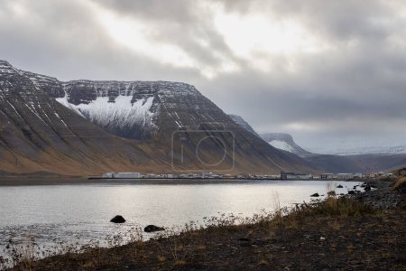Wild coastline of the fjords area Westfjords. Calm water of the Atlantic ocean and majestic mountains with some snow in the autumn. Cloudy sky. Area of Isafjordur, North-West Iceland.