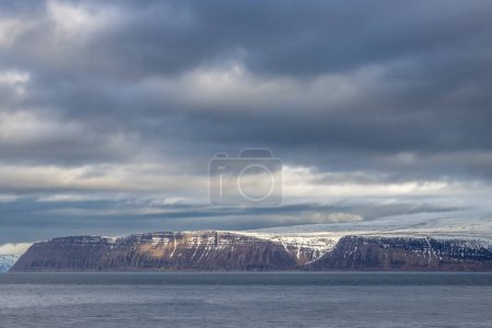 Foto de Costa salvaje de la zona de fiordos Westfjords. Aguas tranquilas del océano Atlántico y majestuosas montañas con un poco de nieve en otoño. Cielo nublado. Zona de Isafjordur, noroeste de Islandia. - Imagen libre de derechos