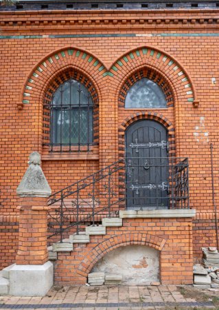 Seitentür zum Gebäude der neugotischen Kirche Mariä Heimsuchung aus orangefarbenen Ziegeln. Weit geöffnetes dunkelbraunes Holztor. Postorna, Breclav, Mähren, Tschechische Republik.