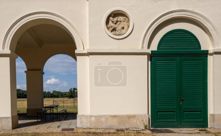 Dark green shutter on the door/window. Stucco with hunting scene. Arcade with view on the park. Sunny day. Pohansko, Breclav, Moravia, Czech republic.