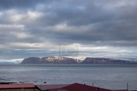 Foto de Aguas tranquilas del océano Atlántico. Montañas altas en la costa en el fondo. Cielo nublado intenso en el otoño. Zona de Isafjordur, Westfjords, Islandia. - Imagen libre de derechos
