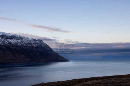 Foto de Montañas tocadas con nieve. Nubes de colores en el cielo azul al atardecer Aguas tranquilas del océano Atlántico en el fiordo. Zona de Westfjords, Isafjordur, Islandia. - Imagen libre de derechos