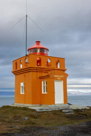 Foto de Fachada naranja brillante del faro. Torre roja con la luz. Cielo nublado en otoño. Construido en la costa del océano Atlántico en la zona de Isafjordur, Westfjords, Islandia. - Imagen libre de derechos
