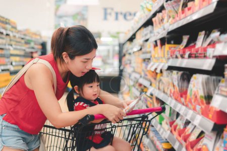 Madre asiática y su hija comprando comida en un enorme supermercado, concepto de compras familiares.