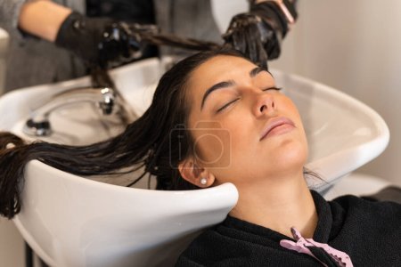 Téléchargez les photos : Crop hairdresser washing hair of calm female client with closed eyes in hairdressing salon during haircut procedure - en image libre de droit