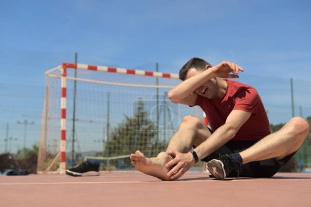 sore man with swollen ankle from injury playing soccer covers his face with his arm while screaming. Has taken off his shoe. Sports physiotherapy medicine concept. High quality photo
