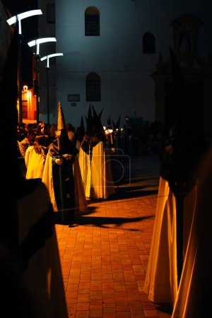Photo for April 8th 2023 - Dona Mencia, Cordoba, Spain. Capiruchos waiting for the Virgin Mary at the door of a church. Spanish Celebration of Holy Week. Vertical shot teal and orange - Royalty Free Image