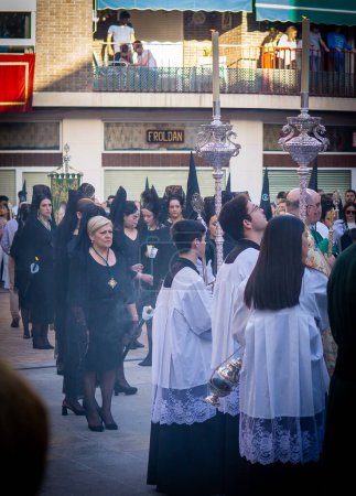 Photo for April 8th 2023 - Dona Mencia, Cordoba, Spain. Devotee woman. Waitress of the Virgin of Solitude waiting for the procession to begin, in front of acolytes and altar boys with incense - Royalty Free Image