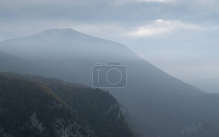 Foto de Mountain slope overgrown with forest against mountain silhouette during gloomy day, mountain landscape - Imagen libre de derechos
