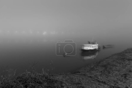 Anchored boats near riverbank in fog at night illuminated with lights, nautical vessel