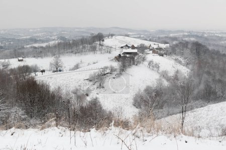 Farm on hill in winter, hilly village landscape during cold day with snow