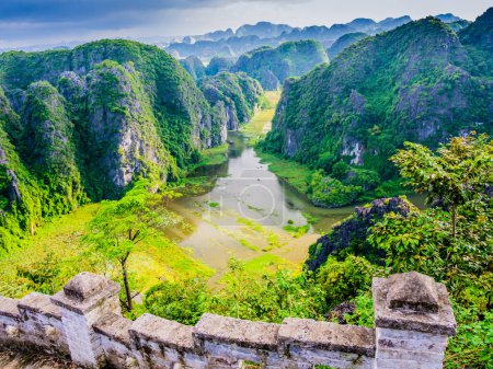 Beeindruckende Karstformationen und Reisfelder in Tam Coc mit der Steintreppe, die den liegenden Drachen im Vordergrund besteigt, Provinz Ninh Binh, Vietnam