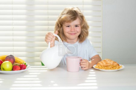 Téléchargez les photos : Pretten enfant versant du lait de vache entier. Un écolier prend son petit déjeuner avant l'école. Portrait de l'enfant assis au bureau à la maison cuisine ont délicieux délicieux petit déjeuner nutritif - en image libre de droit