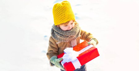 Foto de Niño en ropa de invierno caliente sosteniendo caja de regalo y divertirse al aire libre - Imagen libre de derechos
