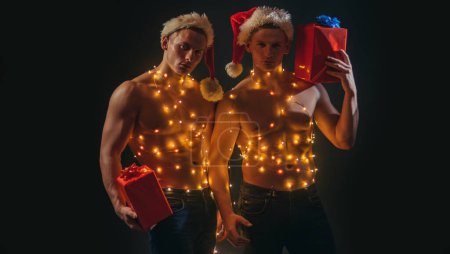 Photo for Christmas party and sex games. Young men hold present for girls. New year strip and gifts for adults. Sexy muscular men. Concept of the twins. Two twin brothers with bare naked body torso - Royalty Free Image