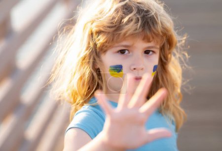 Téléchargez les photos : Arrêtez les gestes de la main de guerre. Drapeau Ukraine sur la joue des enfants. Jeune enfant dans une manifestation avec le drapeau ukrainien. Les enfants protestent. Manifestation des enfants - en image libre de droit