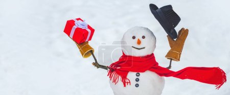 Photo for Christmas snowman with Christmas gift. Hello winter. Happy snowman standing in winter Christmas landscape. Happy smiling snow man on sunny winter day, banne - Royalty Free Image
