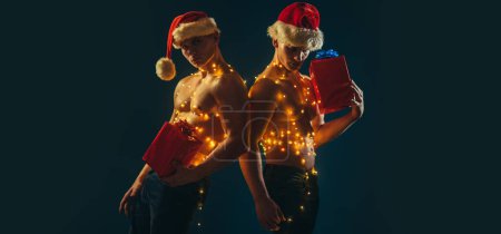 Photo for Young handsome santa man with sexy muscular athletic strong body has bare torso and strong belly holding christmas gift. Two twin brothers with bare naked body torso - Royalty Free Image