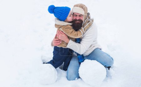 Foto de Papá e hijo sonriendo y abrazándose. Mejor juego de invierno para la familia feliz. Padre e hijo haciendo bola de nieve en la nieve. Papá y el niño jugando con bola de nieve en invierno al aire libre - Imagen libre de derechos