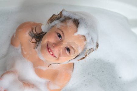 Foto de Champú para niños. Espuma en la cabeza del niño. Niño divirtiéndose en el baño con burbujas. Niño feliz disfrutando del baño. Niño sonriendo en el baño con espuma de jabón. El niño se baña en un baño con espuma - Imagen libre de derechos