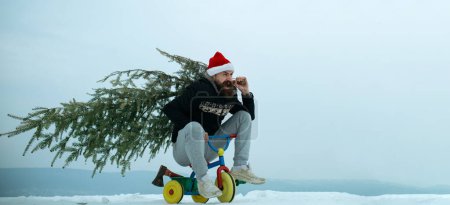 Photo for Crazy winter man on bicycle caring christmas tree. Man with snowman on winter outdoor background. Snow man for winter banner. Funny father on kids bicycle hold christmas tree - Royalty Free Image