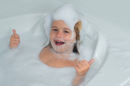 Photo for Kids face in foam. Kid washing with a bubbles in bath. Cute child bathes, lying in a white bath with foam from soap and shampoo - Royalty Free Image