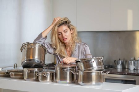 Téléchargez les photos : Femme ennuyée avec beaucoup de casseroles dans la cuisine le matin. Matin de femme femme au foyer - en image libre de droit
