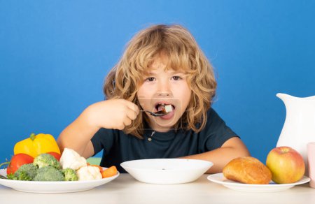 Téléchargez les photos : Petit déjeuner sain pour les enfants. Enfant mangeant des aliments sains sur fond iodé studio. Le bébé mange de la soupe avec une cuillère. Soupe pour enfants - en image libre de droit