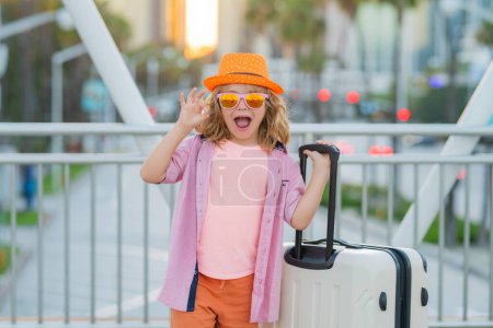 Foto de Un viajero pequeño con maleta. Niño feliz turista con viaje bolsa de viaje. Niño con maleta viajando en la calle de la ciudad al aire libre - Imagen libre de derechos