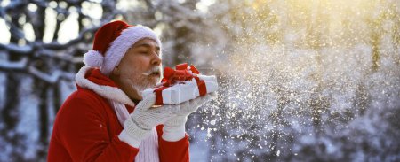 Photo for Santa read Christmas blow snow from Christmas gift. Santa grandfather with Christmas gift outdoor. Elderly santa with gifts. Gift delivery - Royalty Free Image