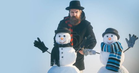 Foto de Hombre de nieve de invierno en sombrero jugar con muñeco de nieve al aire libre. Hombre con muñeco de nieve en invierno fondo al aire libre. Hombre de nieve para bandera de invierno - Imagen libre de derechos