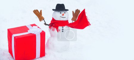 Foto de Muñeco de nieve con gran regalo. Feliz Navidad y feliz año nuevo tarjeta de felicitación. Tarjeta de felicitación de arte festivo con muñecos de nieve. Gift presenta el concepto. Regalo de muñeco de nieve. Regalos de entrega y emociones de regalo - Imagen libre de derechos