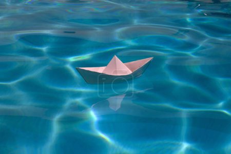 Photo for Paper boat sailing on blue water surface. Paper boat on the sea background. Origami paper boat sailing on water causing waves and ripples - Royalty Free Image