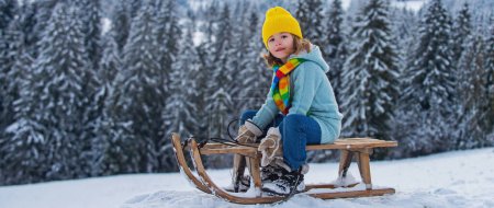 Foto de Niño divirtiéndose con un trineo en el paisaje de invierno. Lindos niños jugando en una nieve en el paisaje natural nevado. Actividades de invierno para niños - Imagen libre de derechos