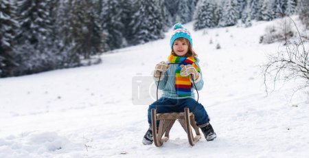 Photo for Funny boy having fun with a sleigh in winter. Cute child play in a snow. Winter activities for kids - Royalty Free Image
