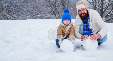Téléchargez les photos : Mignon petit garçon enfant et père heureux sur un terrain enneigé en plein air. Père et fils faisant boule de neige dans la neige. Papa et enfant jouant avec boule de neige en hiver en plein air - en image libre de droit