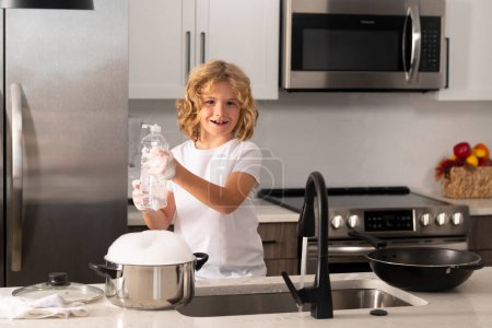 Téléchargez les photos : Lave-vaisselle pour enfants dans la cuisine intérieure. Enfant aidant ses parents avec les travaux ménagers. Mignon garçon drôle lavant la vaisselle dans la cuisine. Américain enfant apprentissage domestique corvées à la maison - en image libre de droit