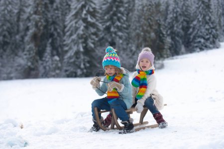 Téléchargez les photos : Enfant garçon et petite fille profitant d'une balade en traîneau. Les enfants font de la luge ensemble, jouent dehors dans la neige sur les montagnes en hiver. papier peint Nouvel An, carte de voeux de Noël - en image libre de droit