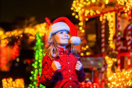 Foto de Decoración de Navidad frente a una casa de noche. Niño cerca de la noche decoración de Navidad en frente de una casa. Noche de Navidad en el fondo de la casa de noche con guirnaldas - Imagen libre de derechos