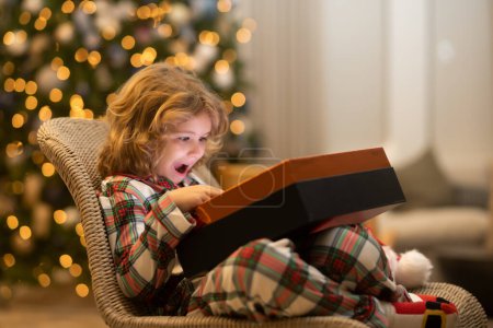 Téléchargez les photos : Surprise enfant ouverture boîte cadeau de Noël. Enfant se préparant pour les vacances de Noël et du Nouvel An - en image libre de droit
